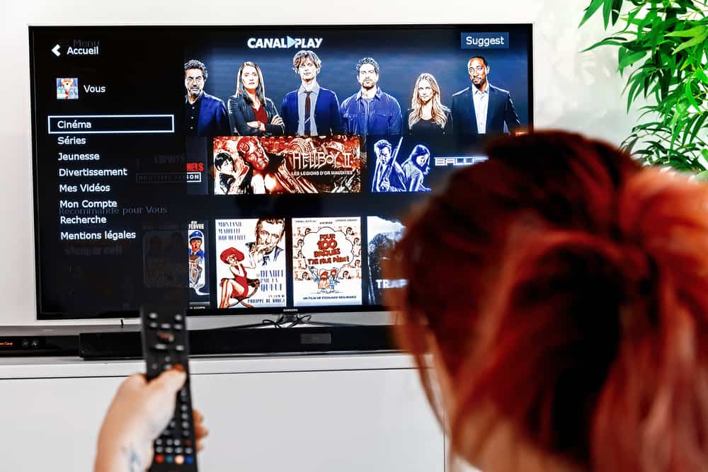 Woman holding a television remote control and watching homepage of canalplay. CanalPlay is a paid French Internet service for the distribution of video files