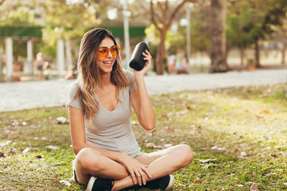 Young beautiful woman enjoying the music at outdoor park. Woman listening music by wireless speaker at outdoor park