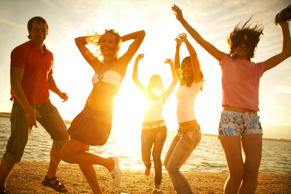 Group of happy young dancing at the beach on beautiful summer sunset